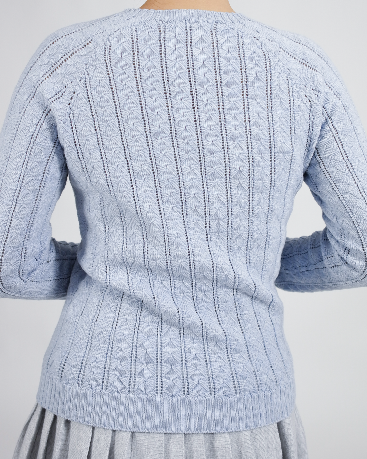 Light blue knitted sweater with cable pattern on a plain background