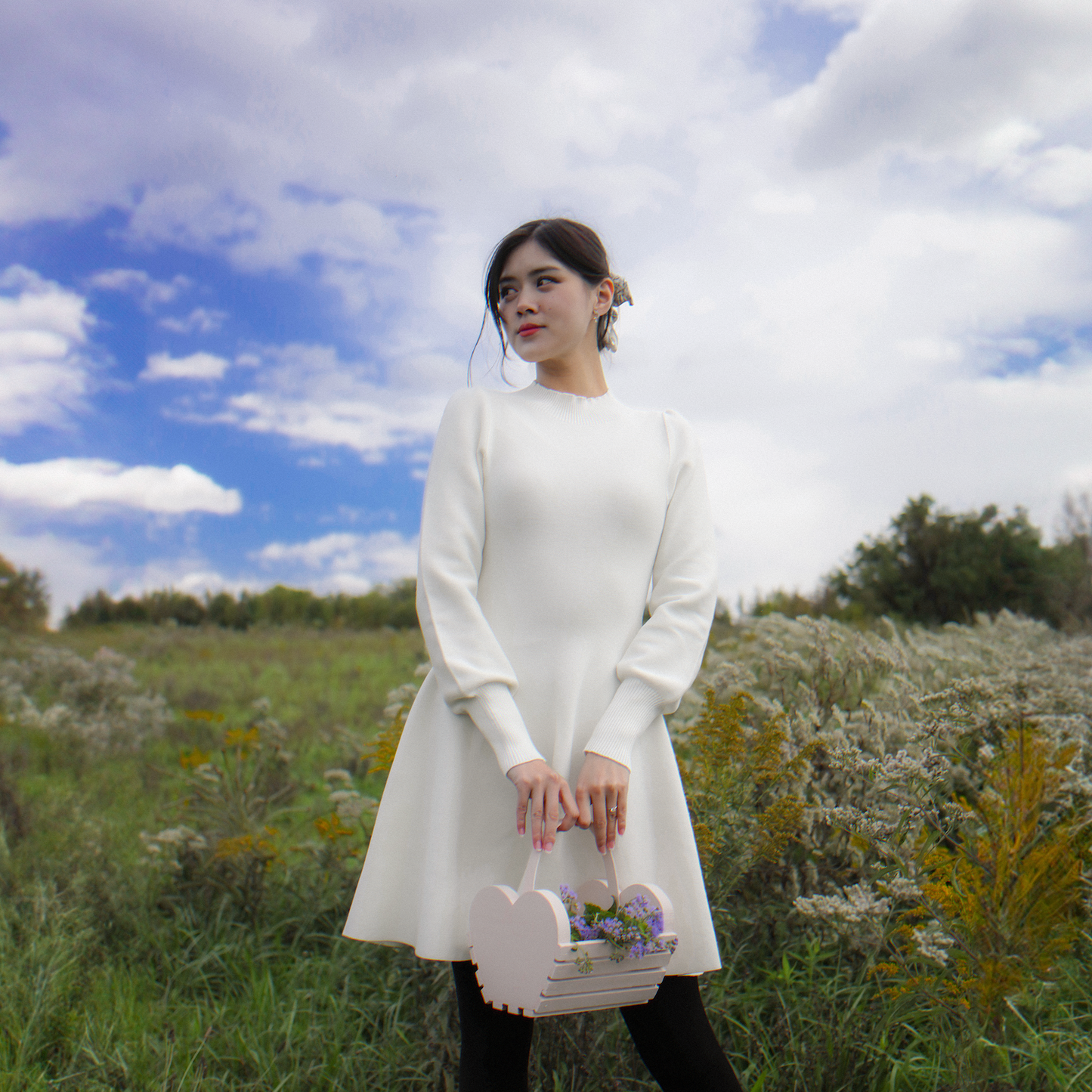 Girl in white long sleeve sweater dress standing in a meadow