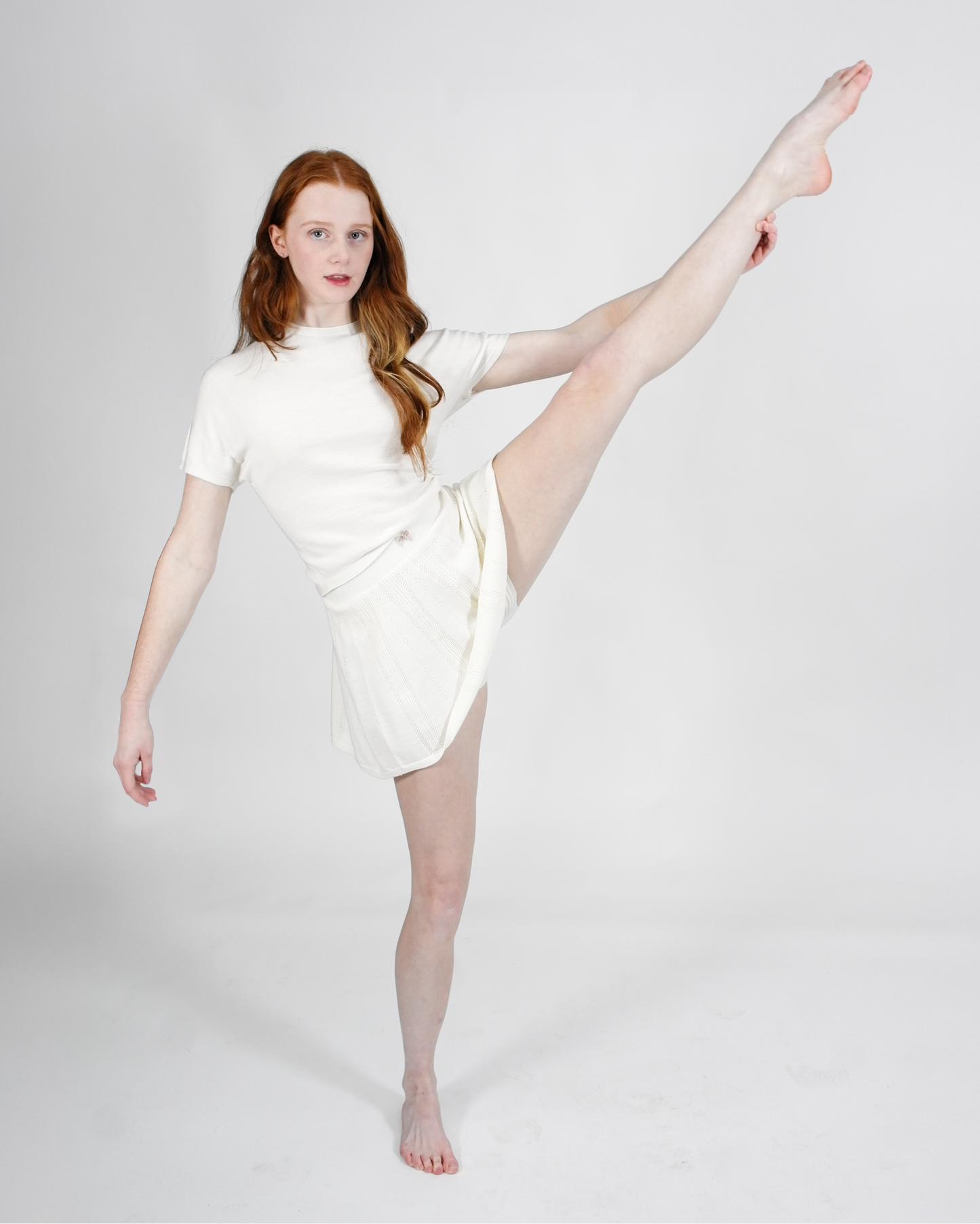 Woman in a white dress posing with one leg lifted on a plain background