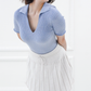 Close three-quarter view of the Corinne ribbed cotton knit polo in Cielo blue, styled with a white pleated skirt