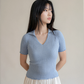 Woman wearing a light blue ribbed knit top against a plain background