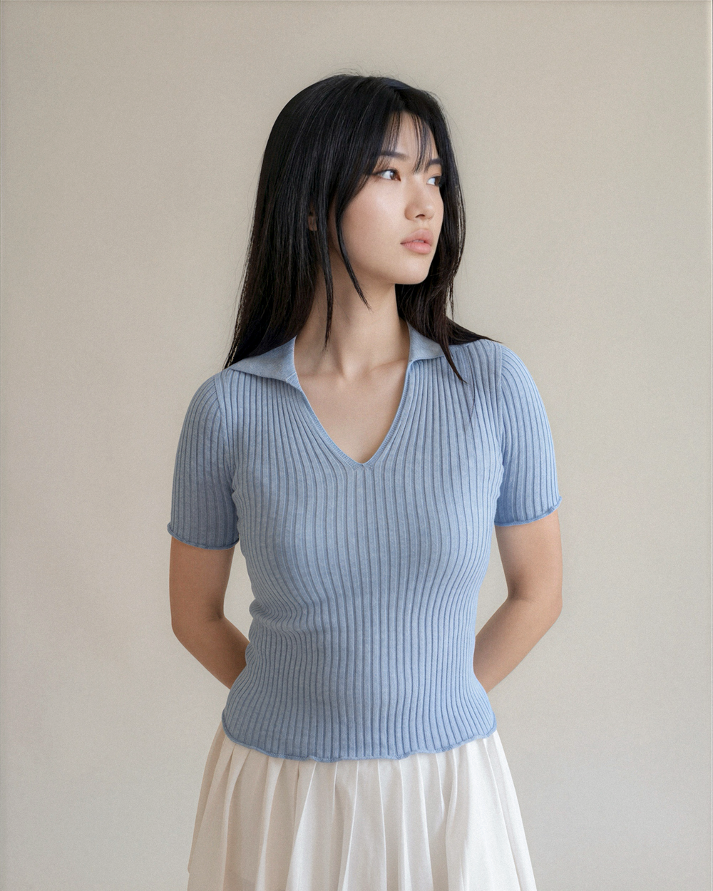 Woman wearing a light blue ribbed knit top against a plain background