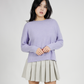 Woman wearing a light purple sweater and pleated skirt on a white background