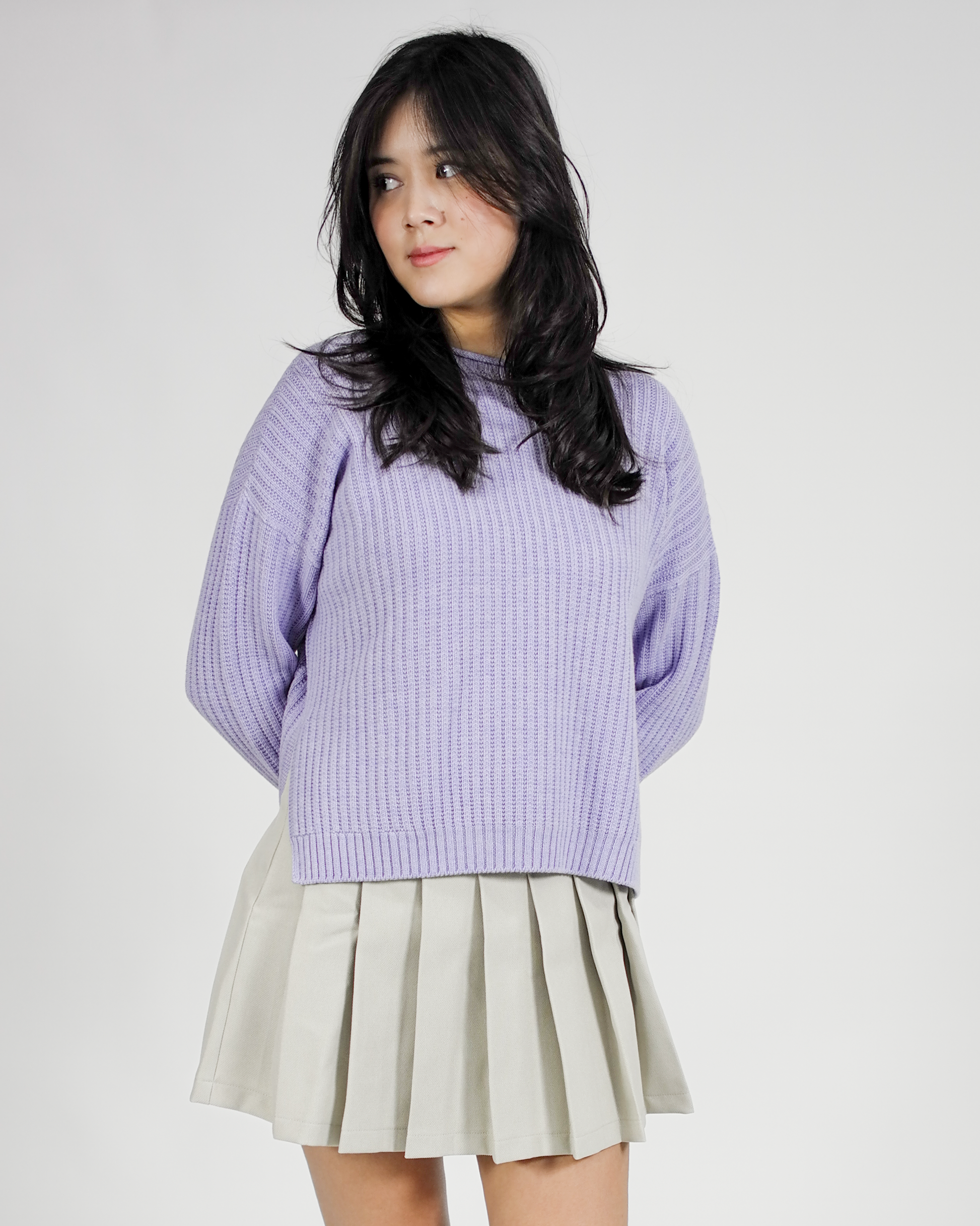 Person wearing a purple sweater and beige pleated skirt on a white background