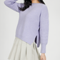 Person wearing a light purple sweater and beige skirt on a white background