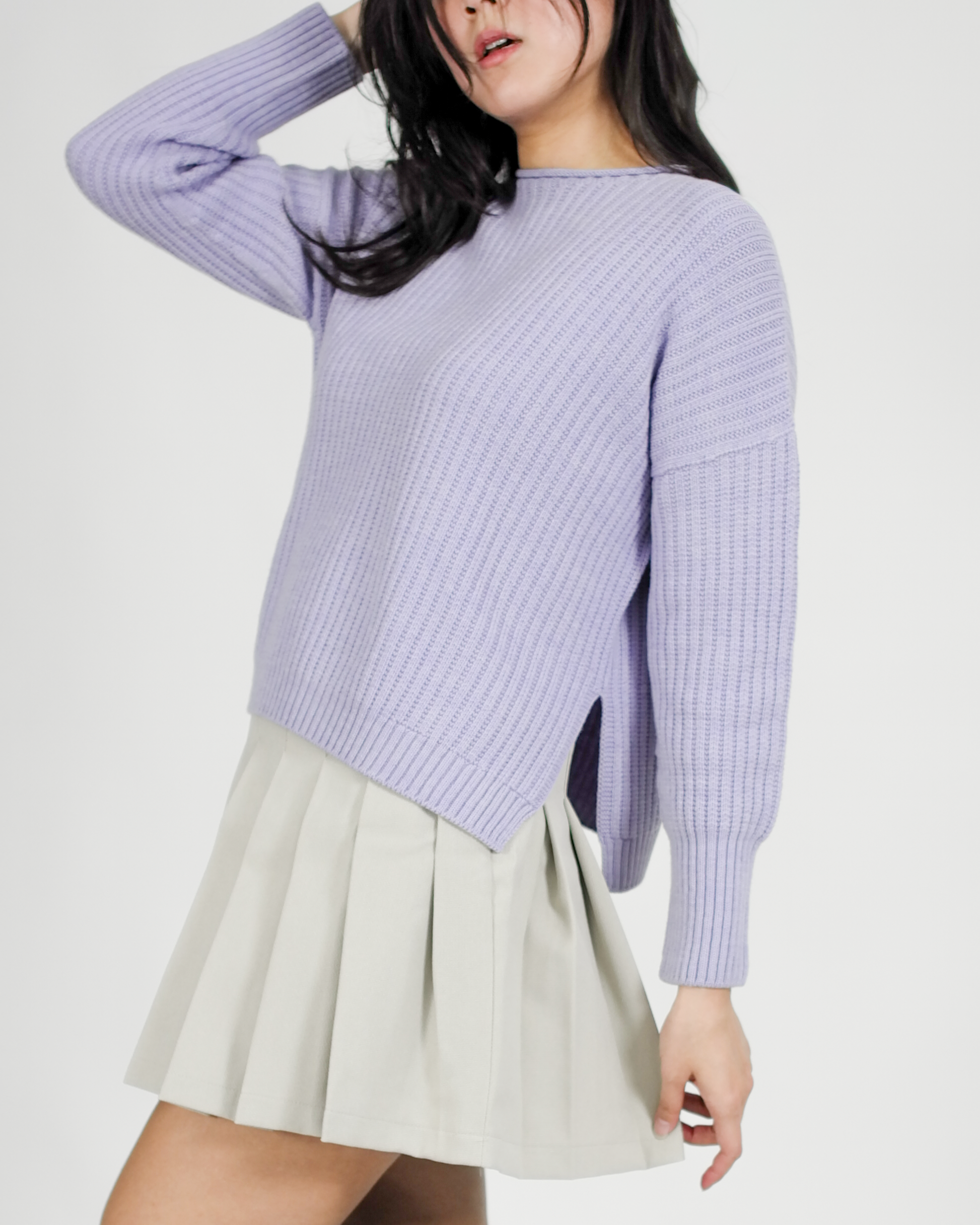 Person wearing a light purple sweater and beige skirt on a white background
