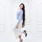 Model wearing the Jasmin cotton cardigan in Cielo blue with a white knit dress, full-length side view