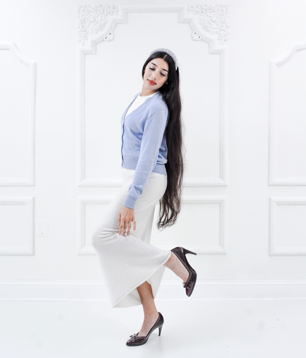 Model wearing the Jasmin cotton cardigan in Cielo blue with a white knit dress, full-length side view