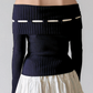 Navy off-shoulder sweater with white accents worn by a person on a plain background
