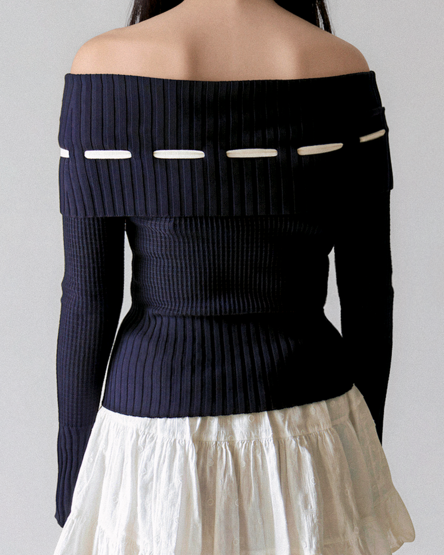 Navy off-shoulder sweater with white accents worn by a person on a plain background