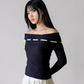 Woman wearing a dark blue off-shoulder top with white trim on a gray background