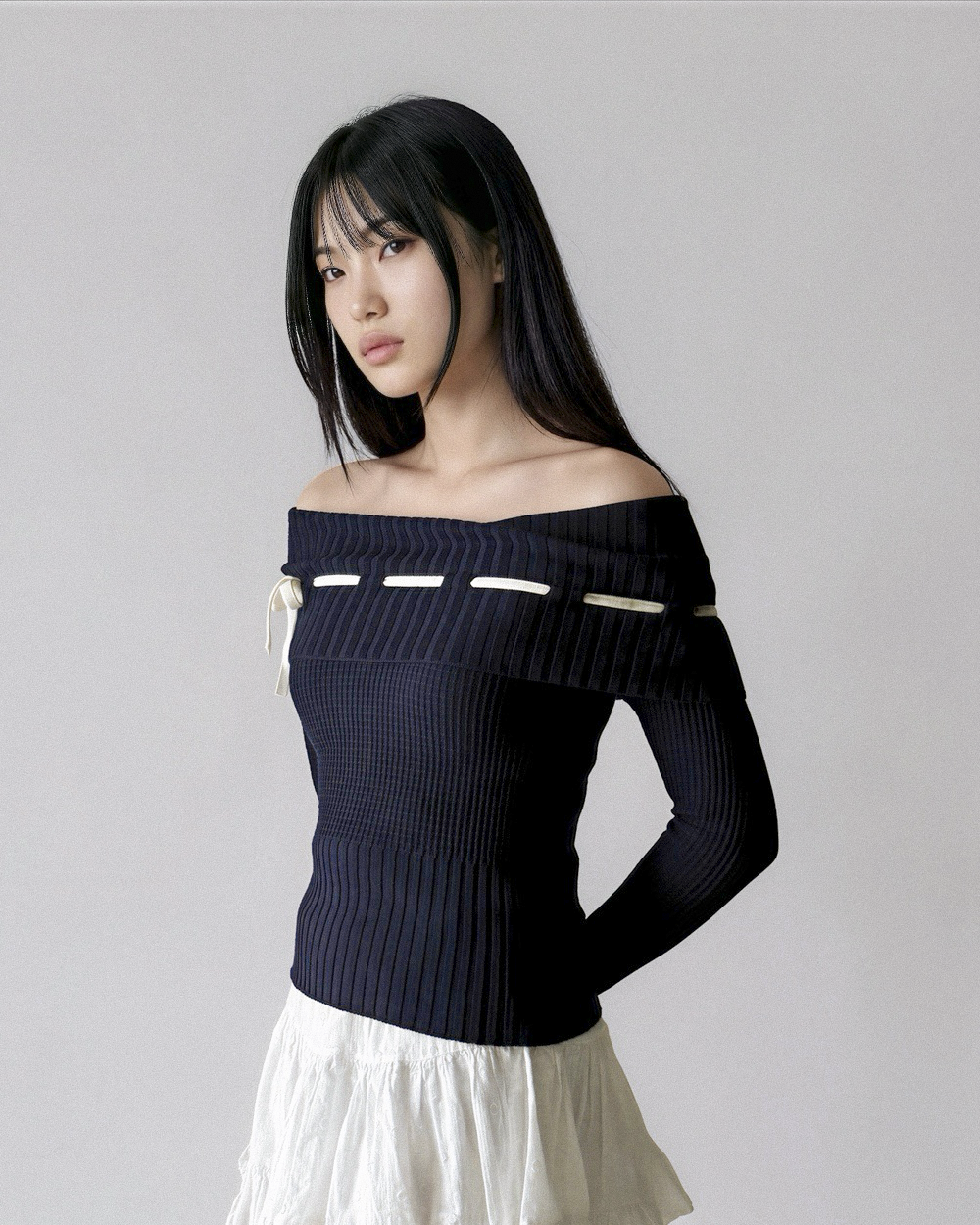 Woman wearing a dark blue off-shoulder top with white trim on a gray background