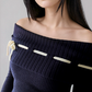 Woman wearing a dark blue off-shoulder top with gold accents on a plain background