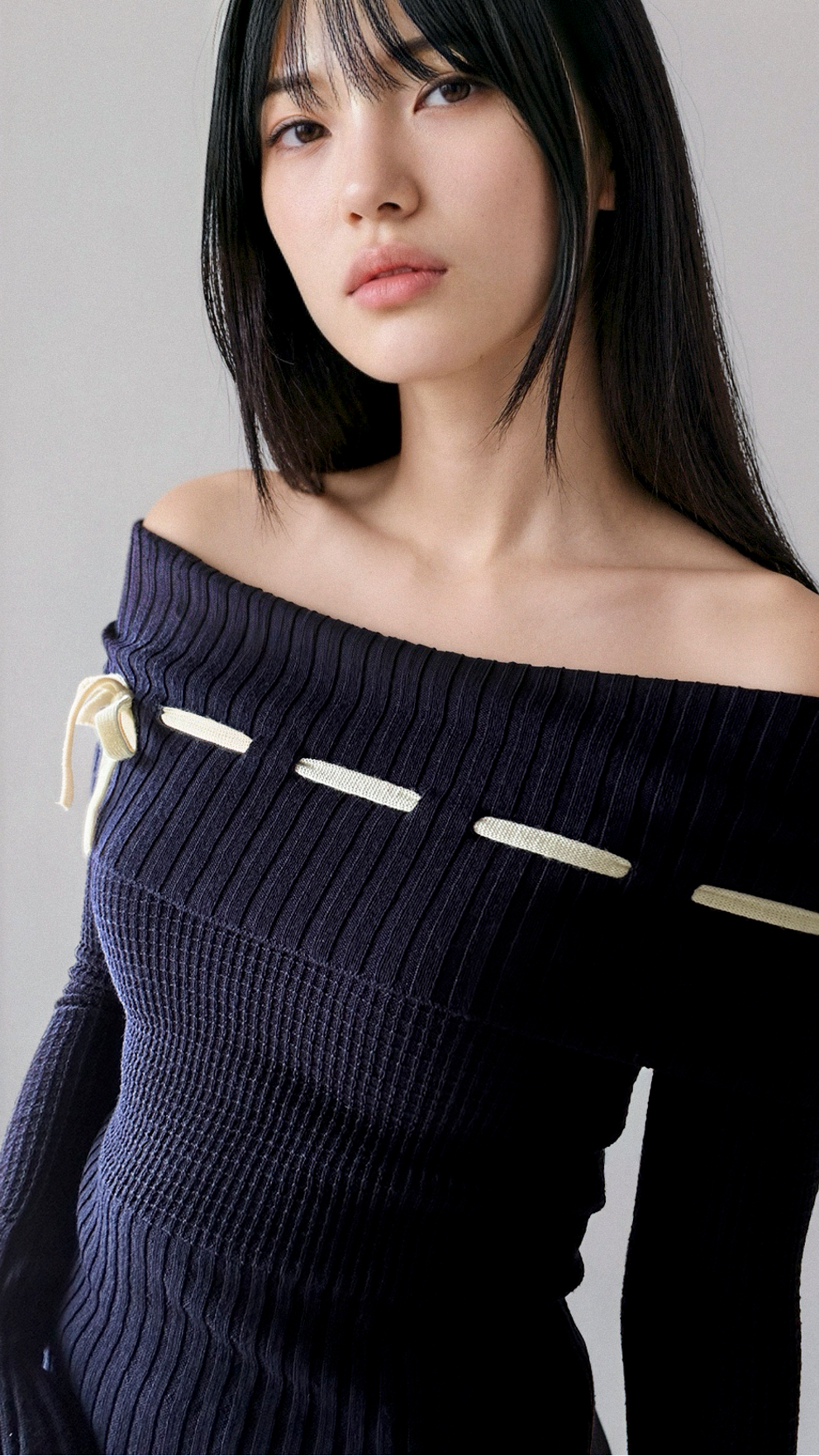 Woman wearing a dark blue off-shoulder top with gold accents on a plain background