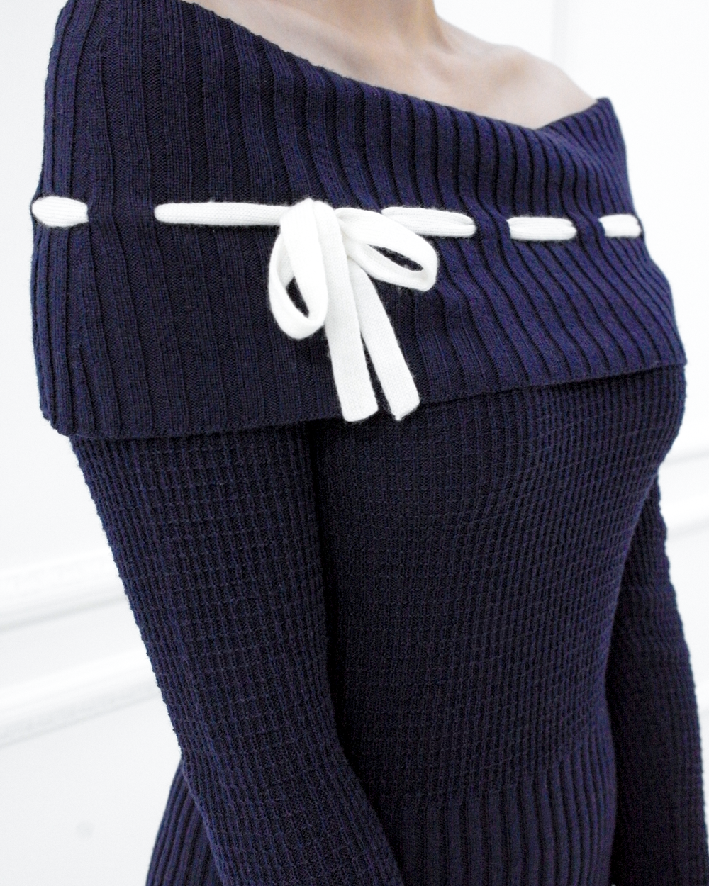 Close-up of the Lisette navy merino off-shoulder top with a white ribbon bow and ribbed foldover neckline