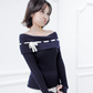 Model wearing the Lisette navy merino off-shoulder top with a white ribbon bow, front three-quarter view