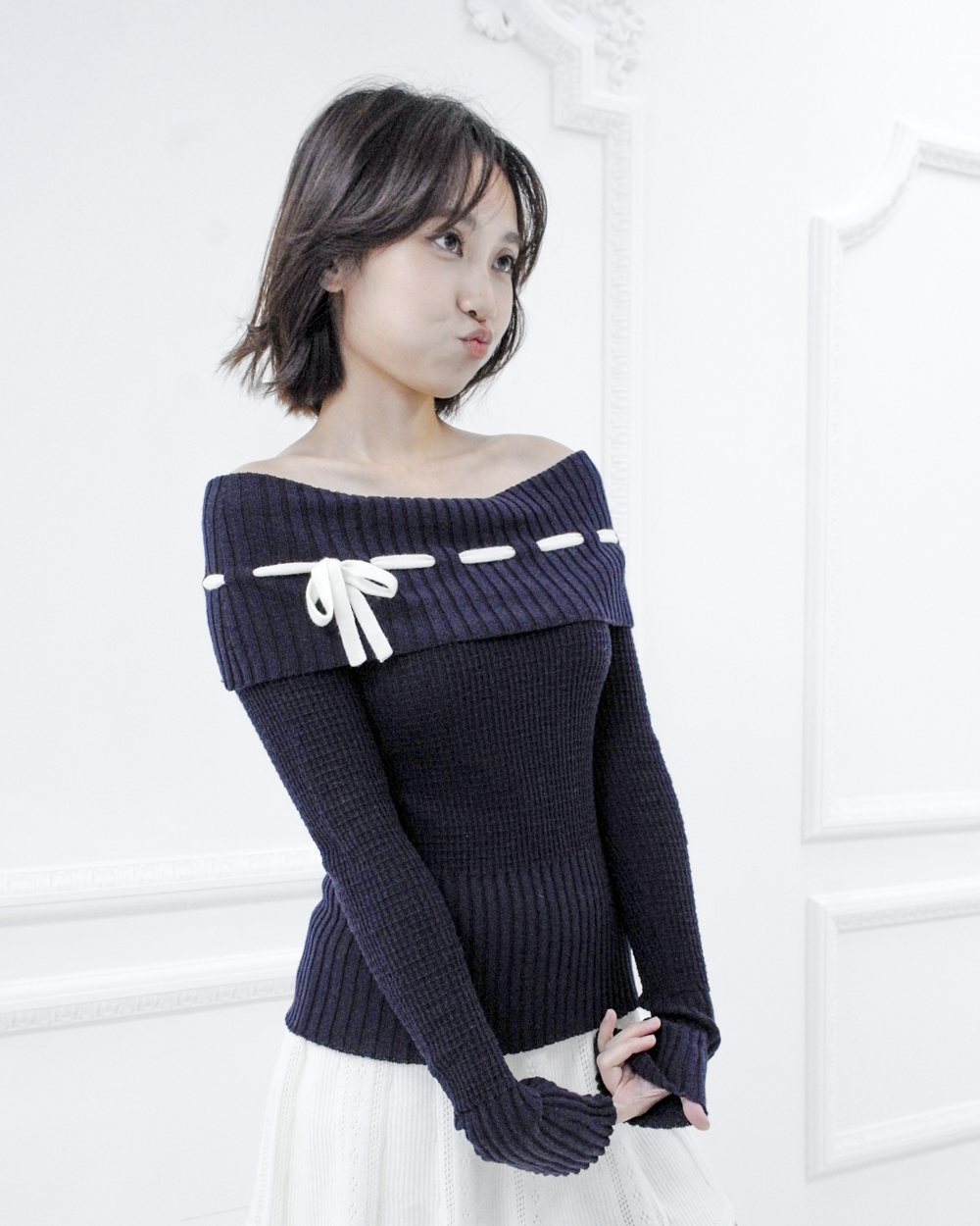 Model wearing the Lisette navy merino off-shoulder top with a white ribbon bow, front three-quarter view
