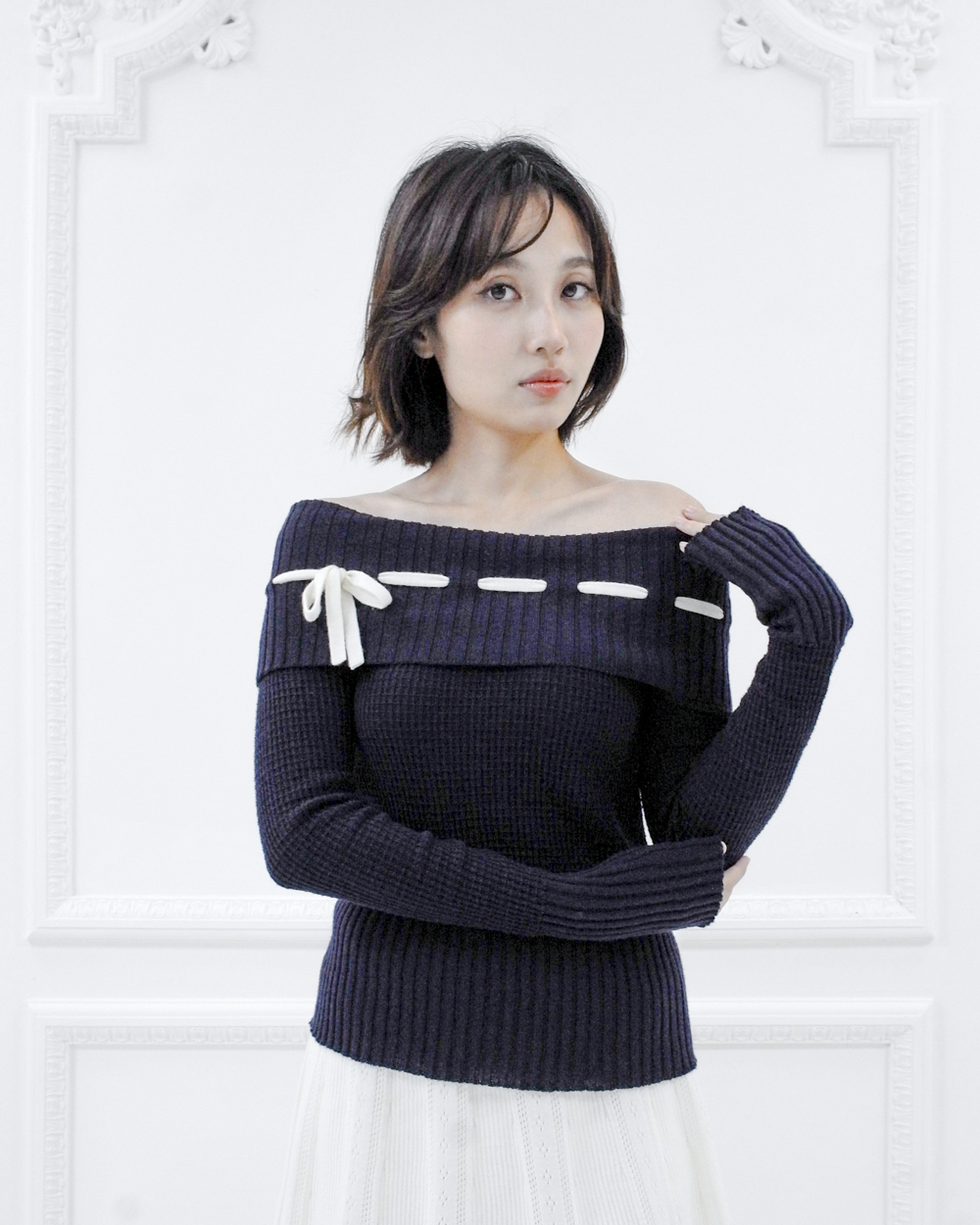 Front view of the Lisette navy merino off-shoulder top styled with a white knit skirt