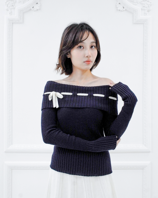Front view of the Lisette navy merino off-shoulder top styled with a white knit skirt