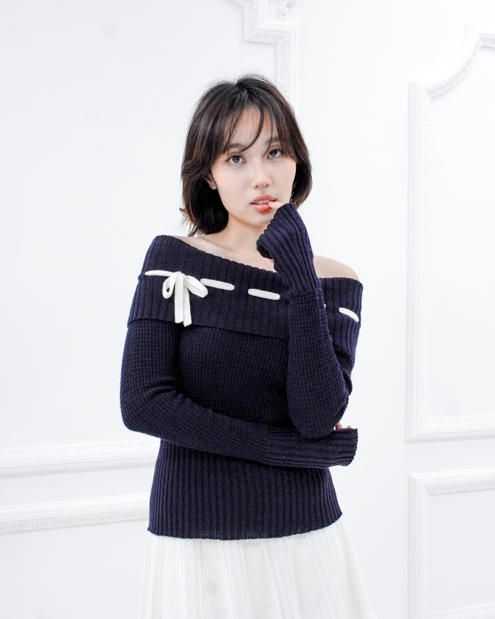 Model wearing the Lisette navy merino off-shoulder top with a white ribbon bow and elongated ribbed cuffs