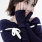 Portrait close-up of the Lisette navy merino off-shoulder top with a white ribbon bow and elongated ribbed cuffs