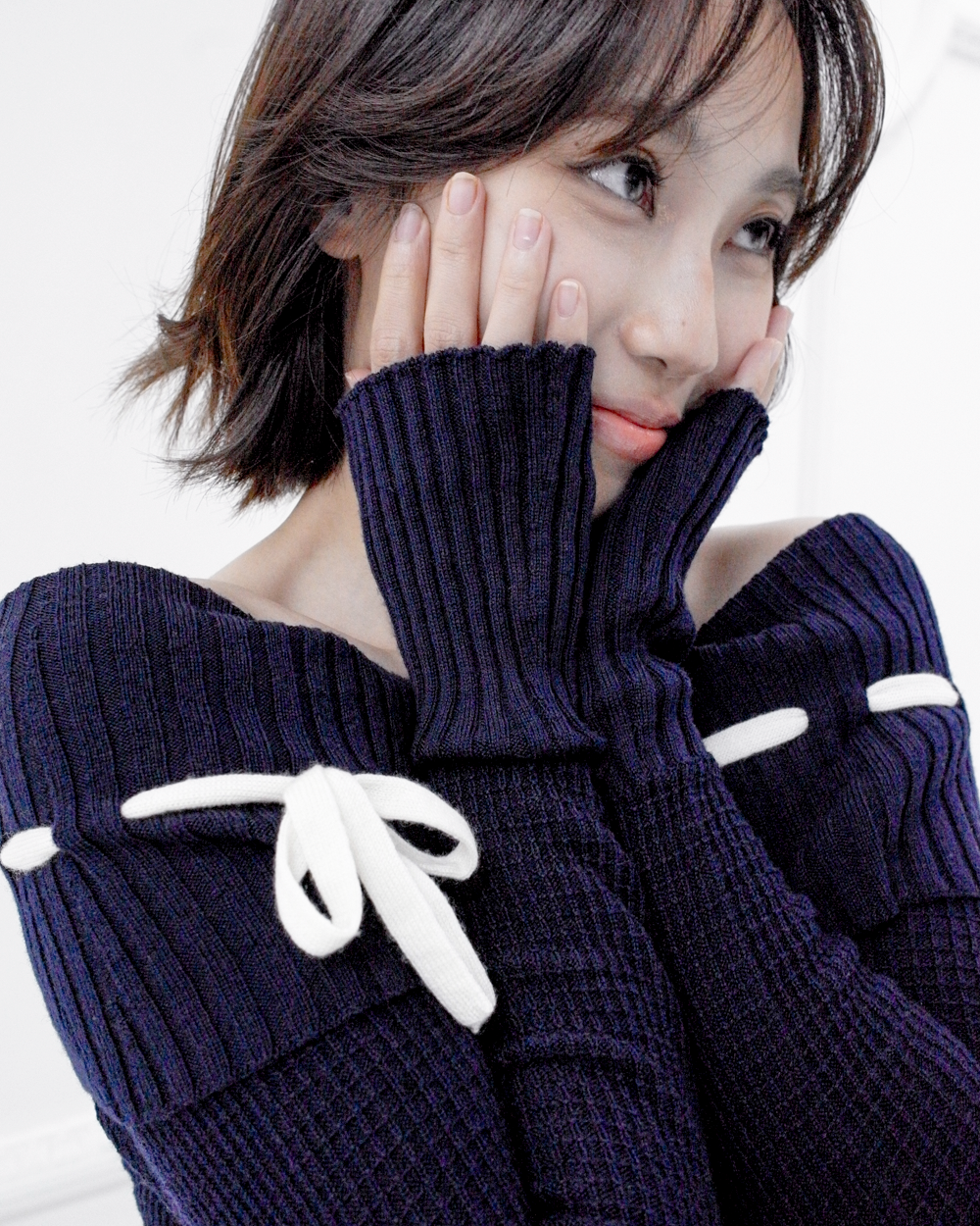 Portrait close-up of the Lisette navy merino off-shoulder top with a white ribbon bow and elongated ribbed cuffs