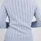 Light blue knitted sweater with cable pattern on a plain background