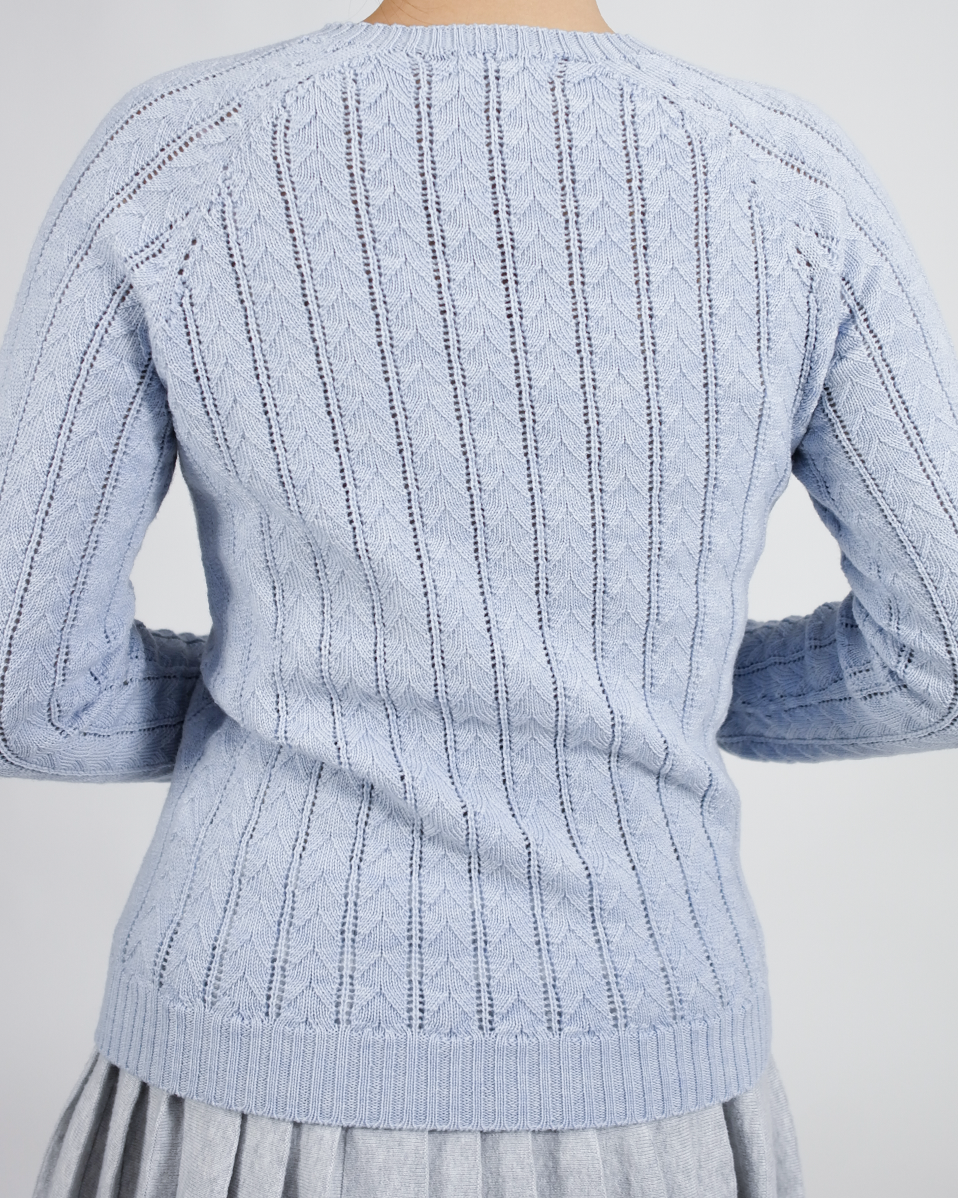 Light blue knitted sweater with cable pattern on a plain background