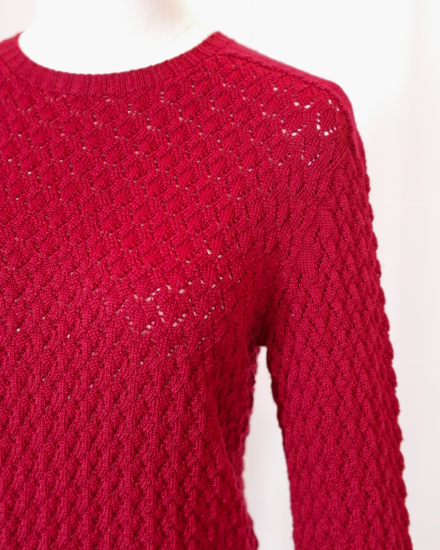 Red pointelle knitted long sleeve sweater on a white background - closeup