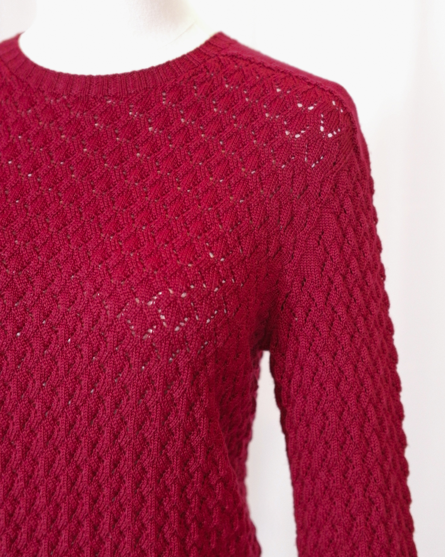 Red pointelle knitted long sleeve sweater on a white background - closeup
