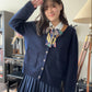 girl wearing dark navy blue cardigan and pleated skirt with a scarf, posing with a salute