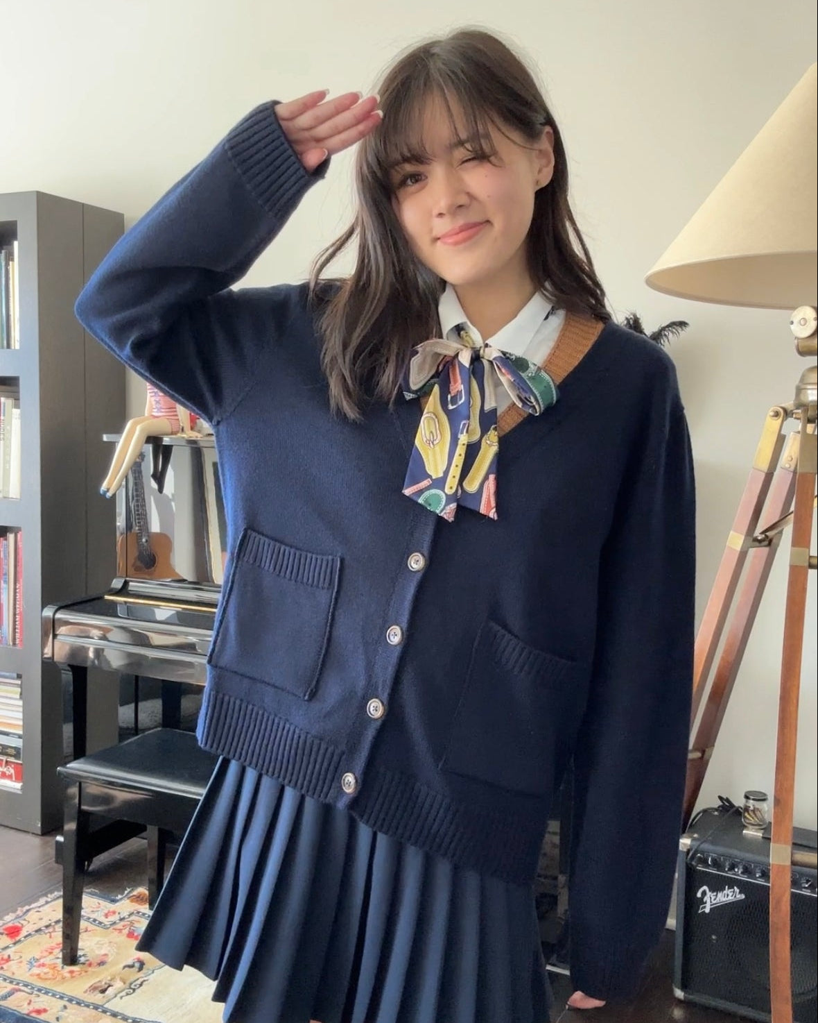 girl wearing dark navy blue cardigan and pleated skirt with a scarf, posing with a salute