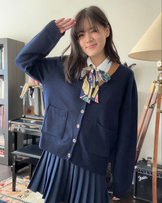 girl wearing dark navy blue cardigan and pleated skirt with a scarf, posing with a salute