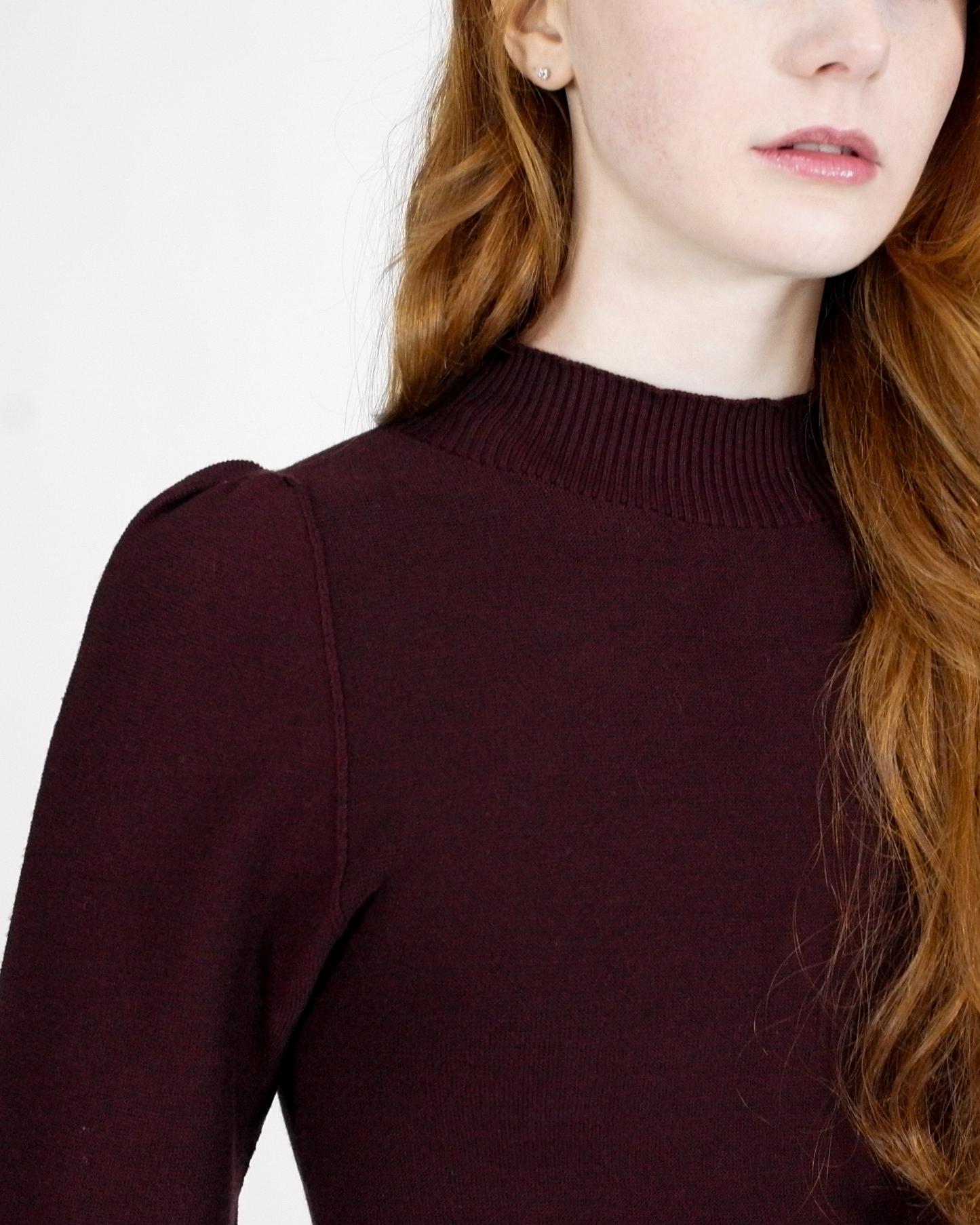 Person wearing a dark maroon sweater against a white background