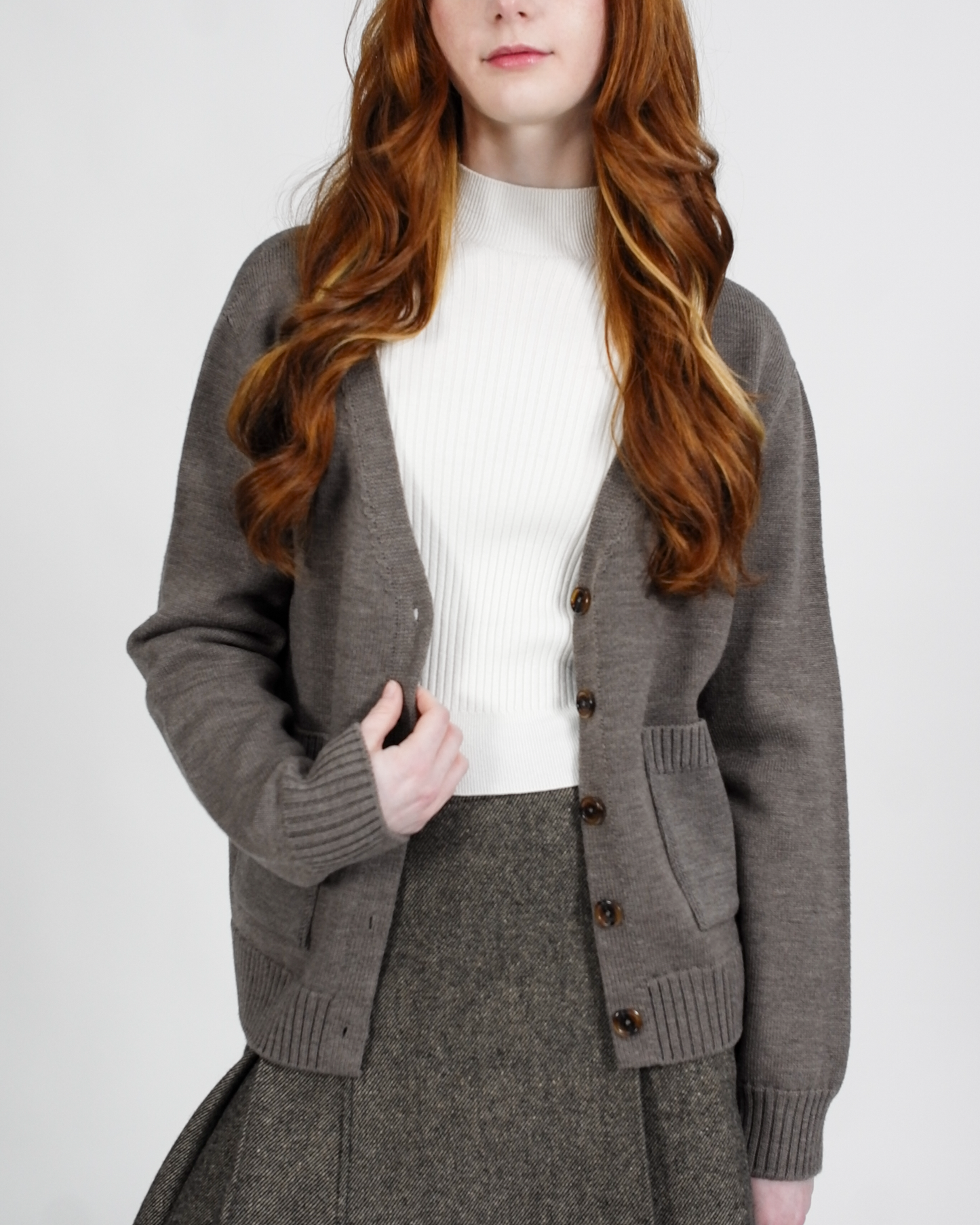 Person wearing a gray cardigan over a white sweater on a plain background