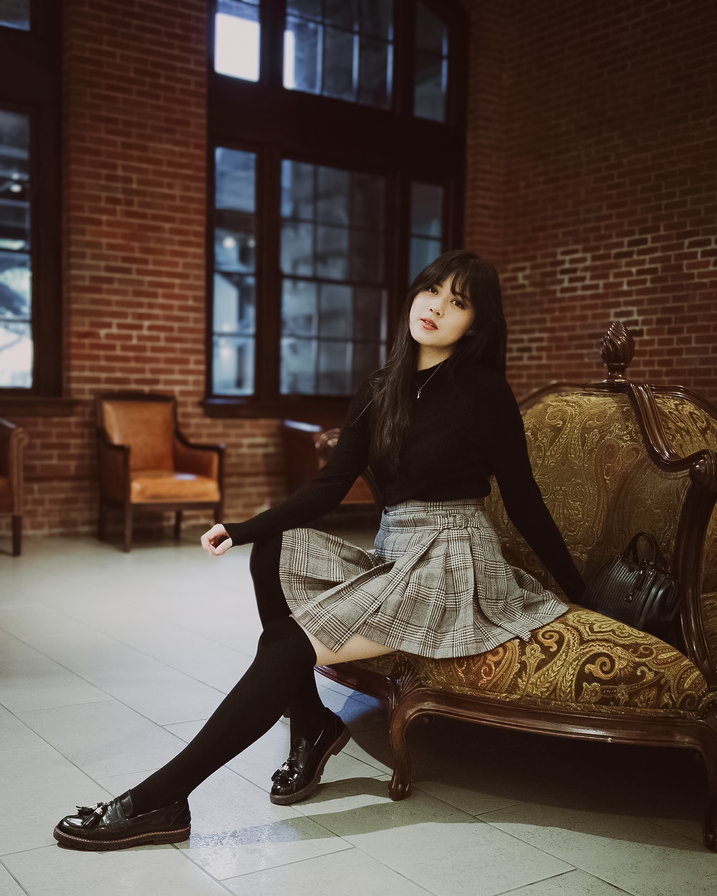 Woman sitting on a ornate couch in a room with brick walls and large windows.