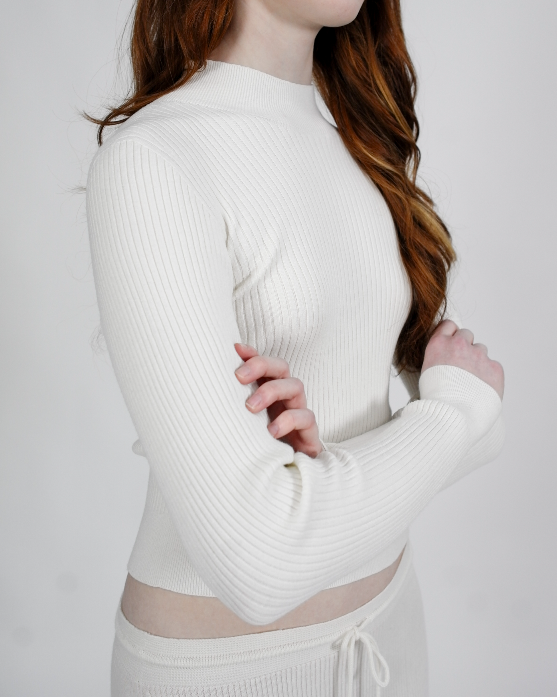 Person wearing a white ribbed long-sleeve top against a plain background