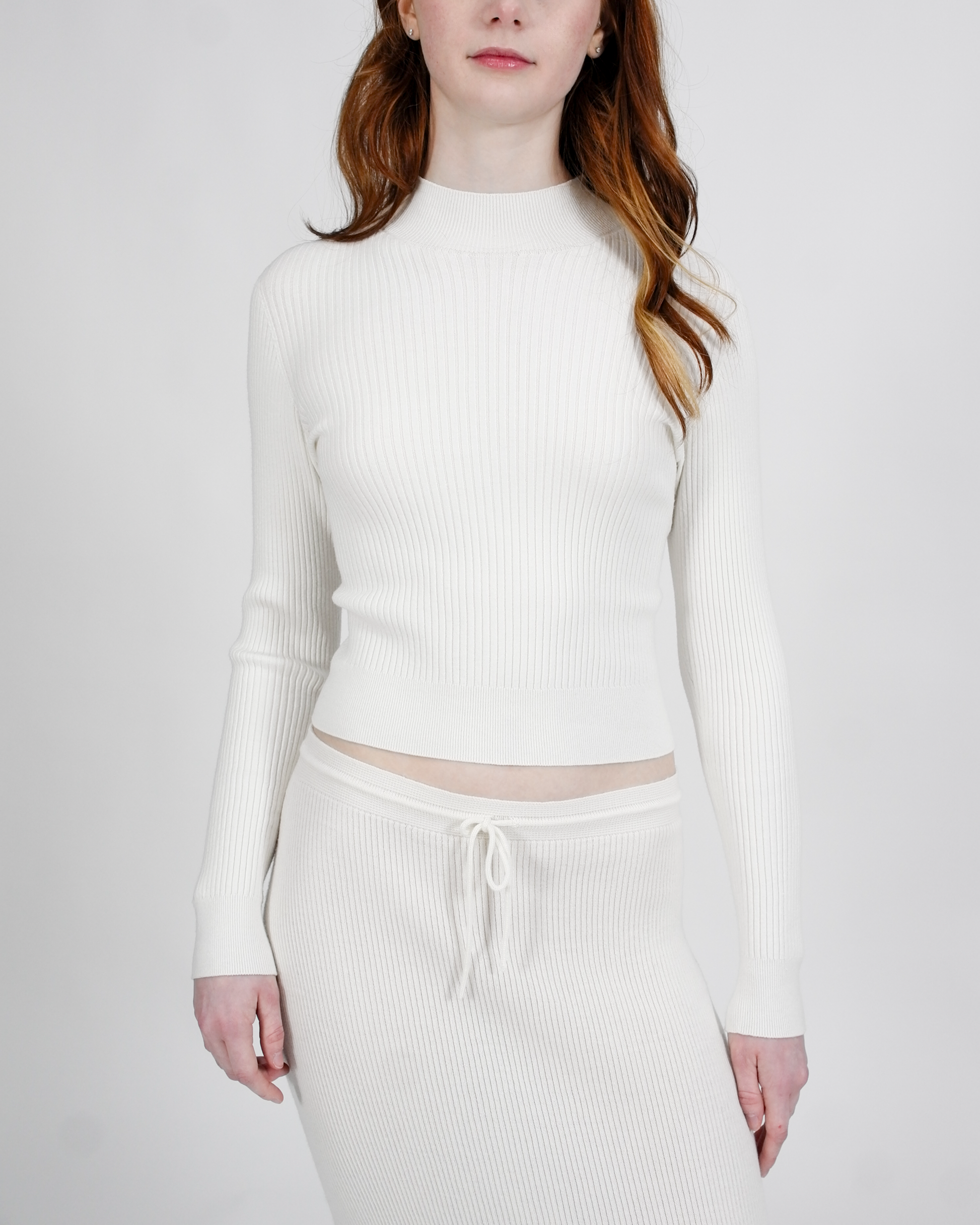 Person wearing a white ribbed long-sleeve top and pants on a plain background