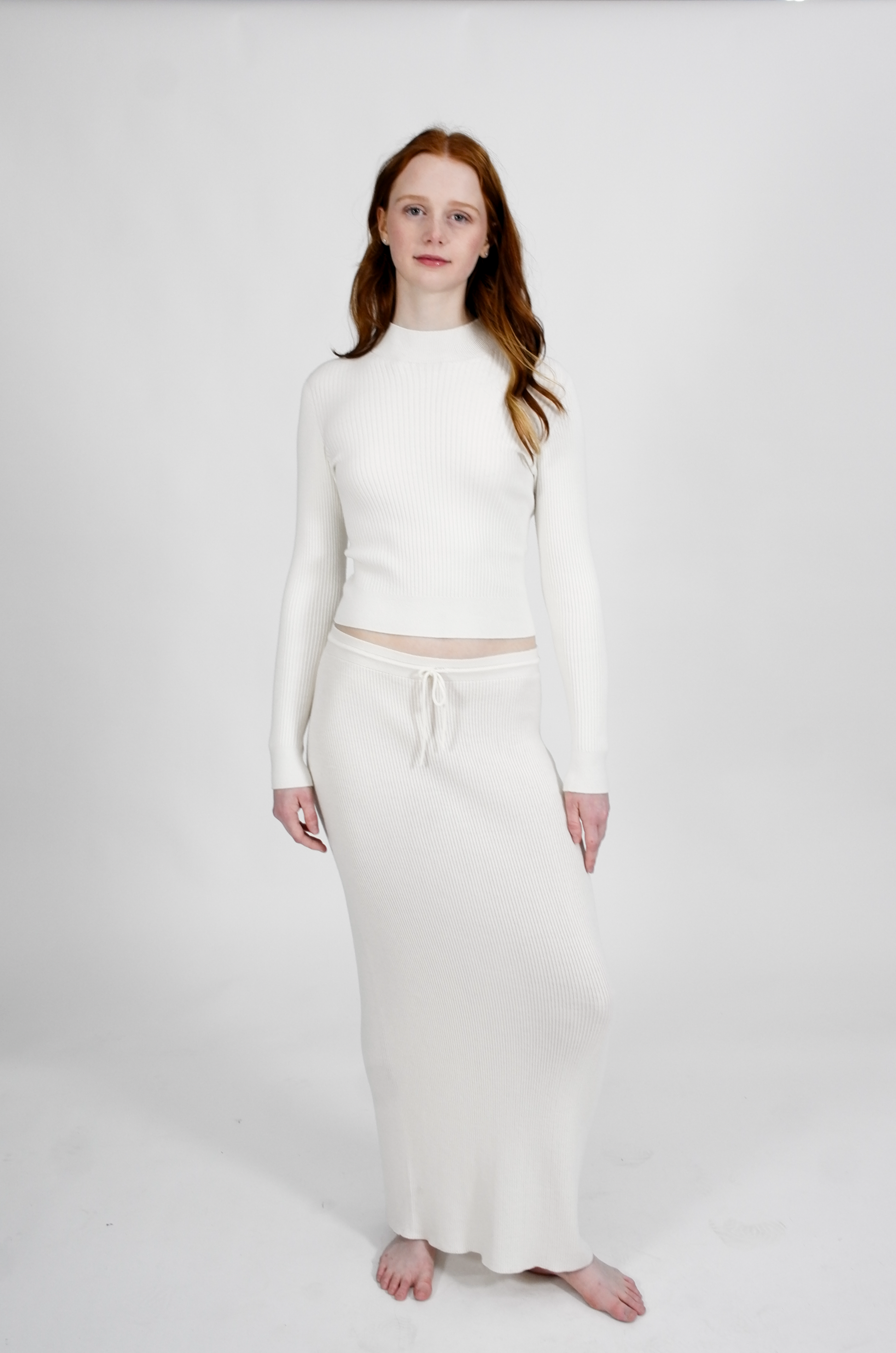 Person wearing a white long-sleeve top and skirt on a plain background